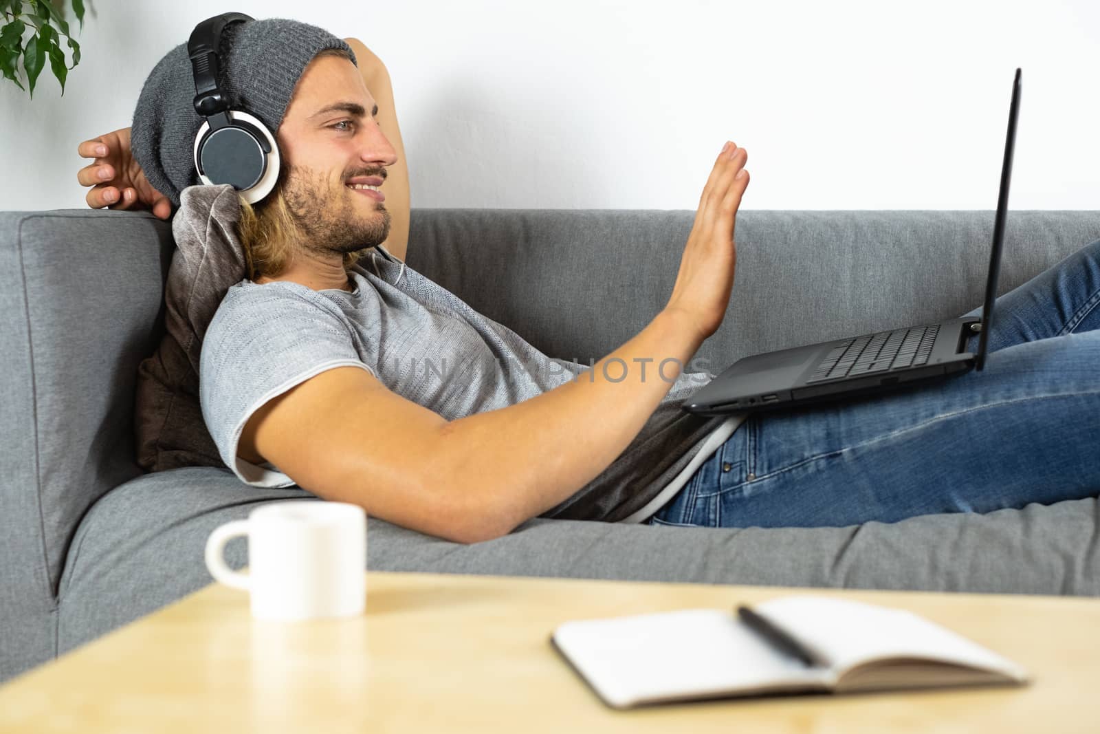 Handsome young business caucasian man working at home using laptop and talking with mobile phone saying hello