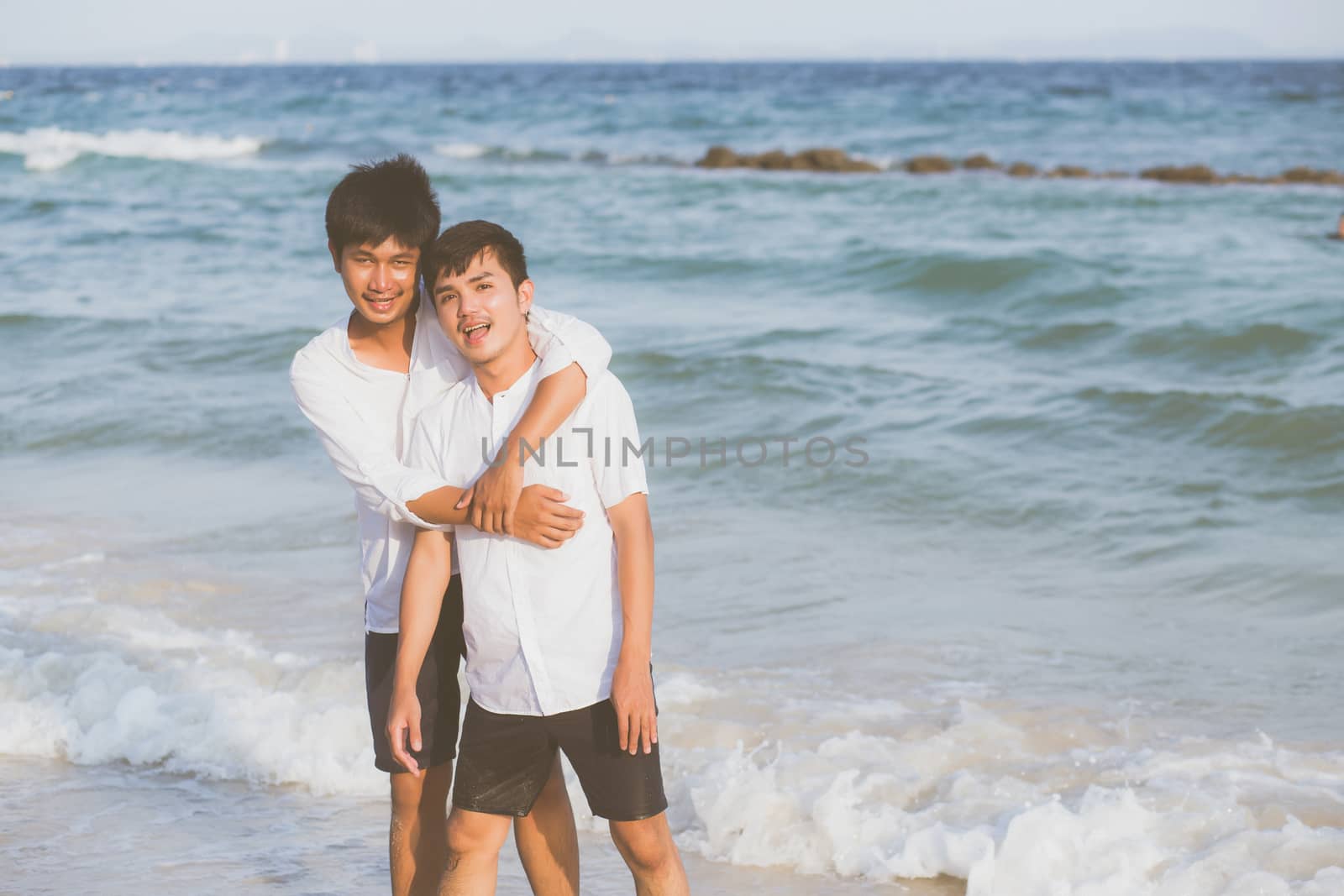 Homosexual portrait young asian couple standing hug together on beach in summer, asia gay going tourism for leisure and relax with romantic and happiness in vacation at sea, LGBT concept.