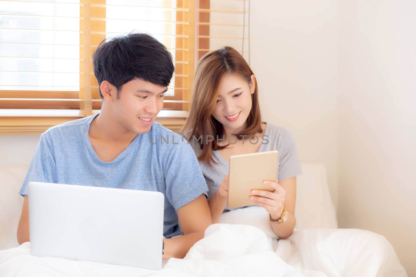 Beautiful young asian couple cheerful freelance working with man using laptop and woman using tablet on couch, family relax and sharing communication together at home, lifestyle concept.