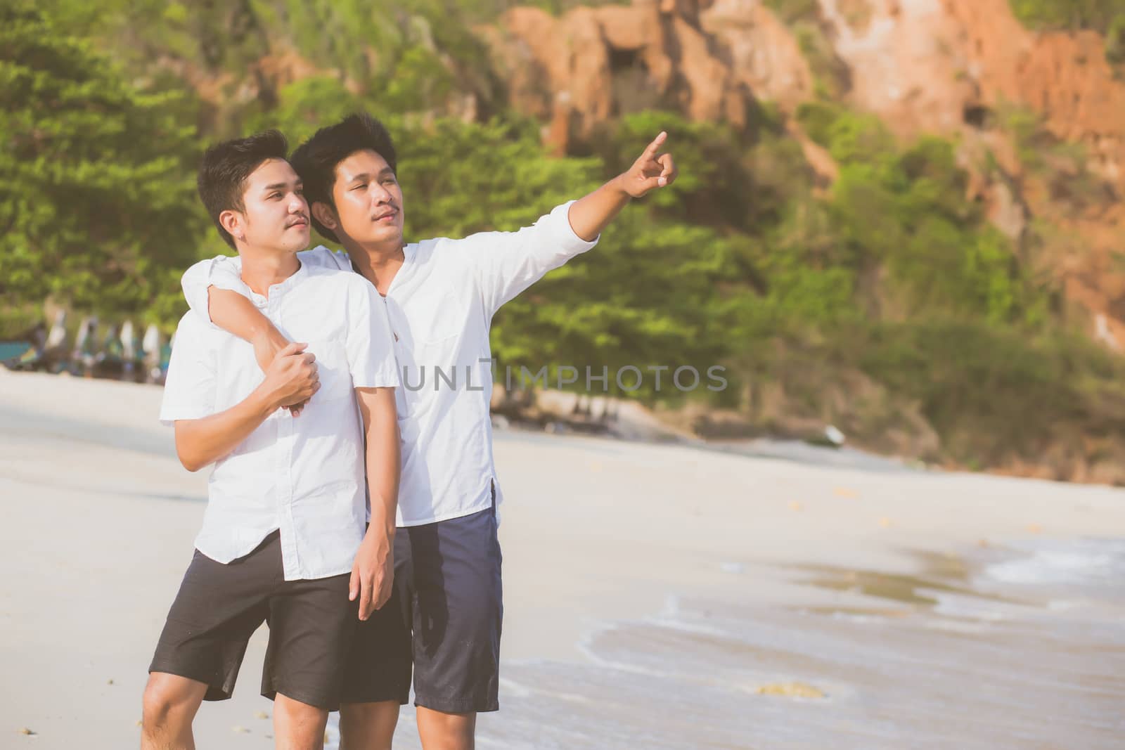 Homosexual portrait young asian couple standing pointing something together on beach in summer, asia gay going sea for leisure with romantic and happy in vacation at sea, LGBT with legal concept.