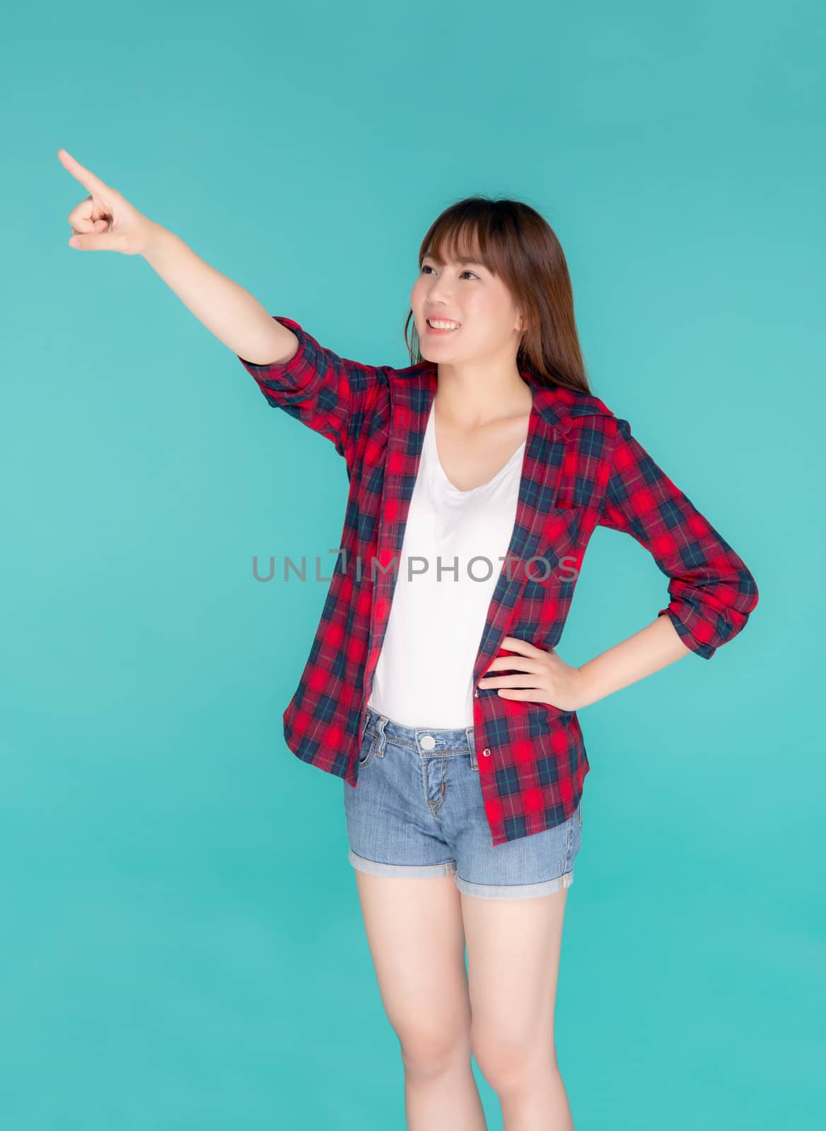 Beautiful portrait young asian woman smiling gesture pointing something and excited summer holiday isolated blue background, asia girl confident and cheerful with journey, travel concept.