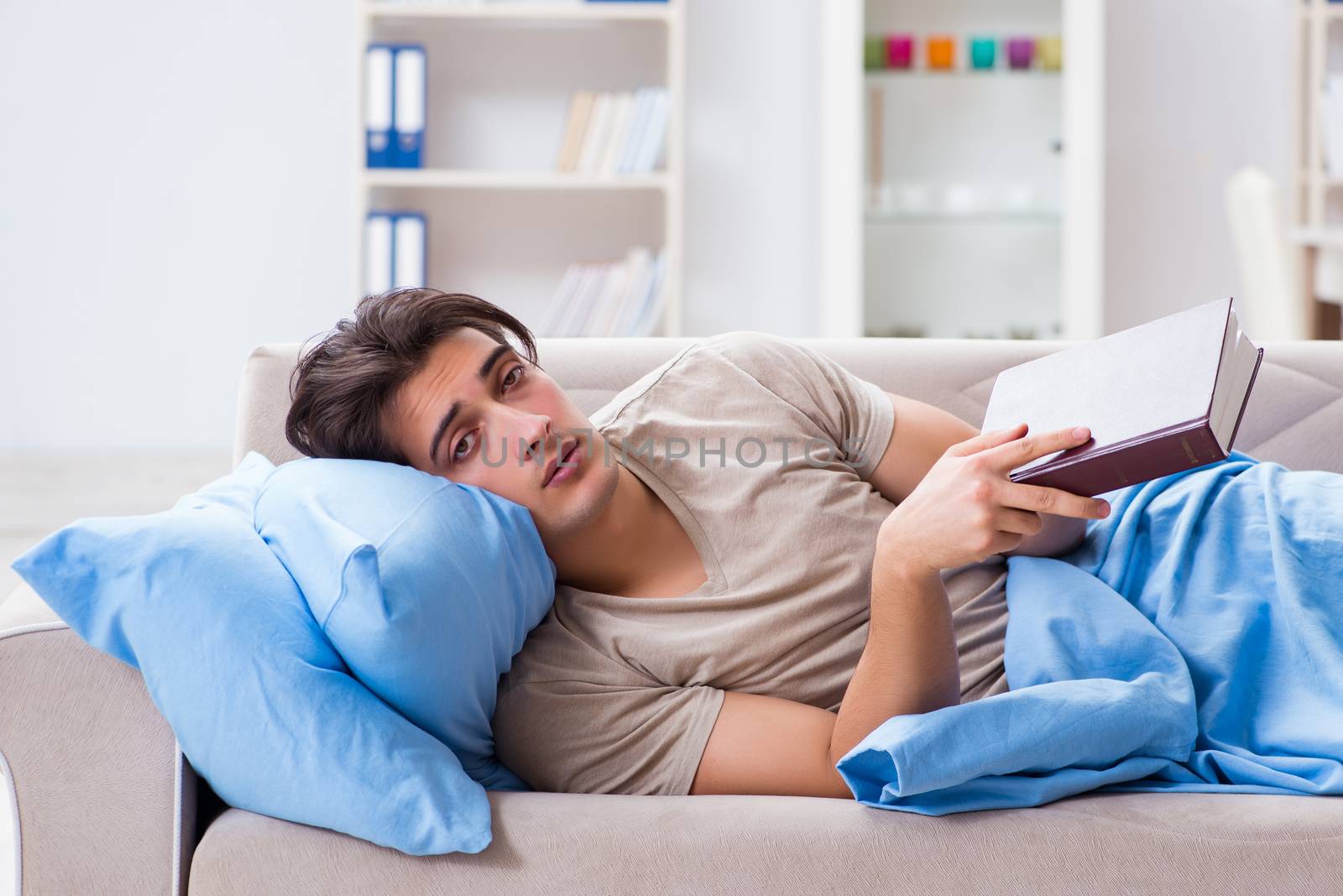 Young student man preparing for college exams in bed with book