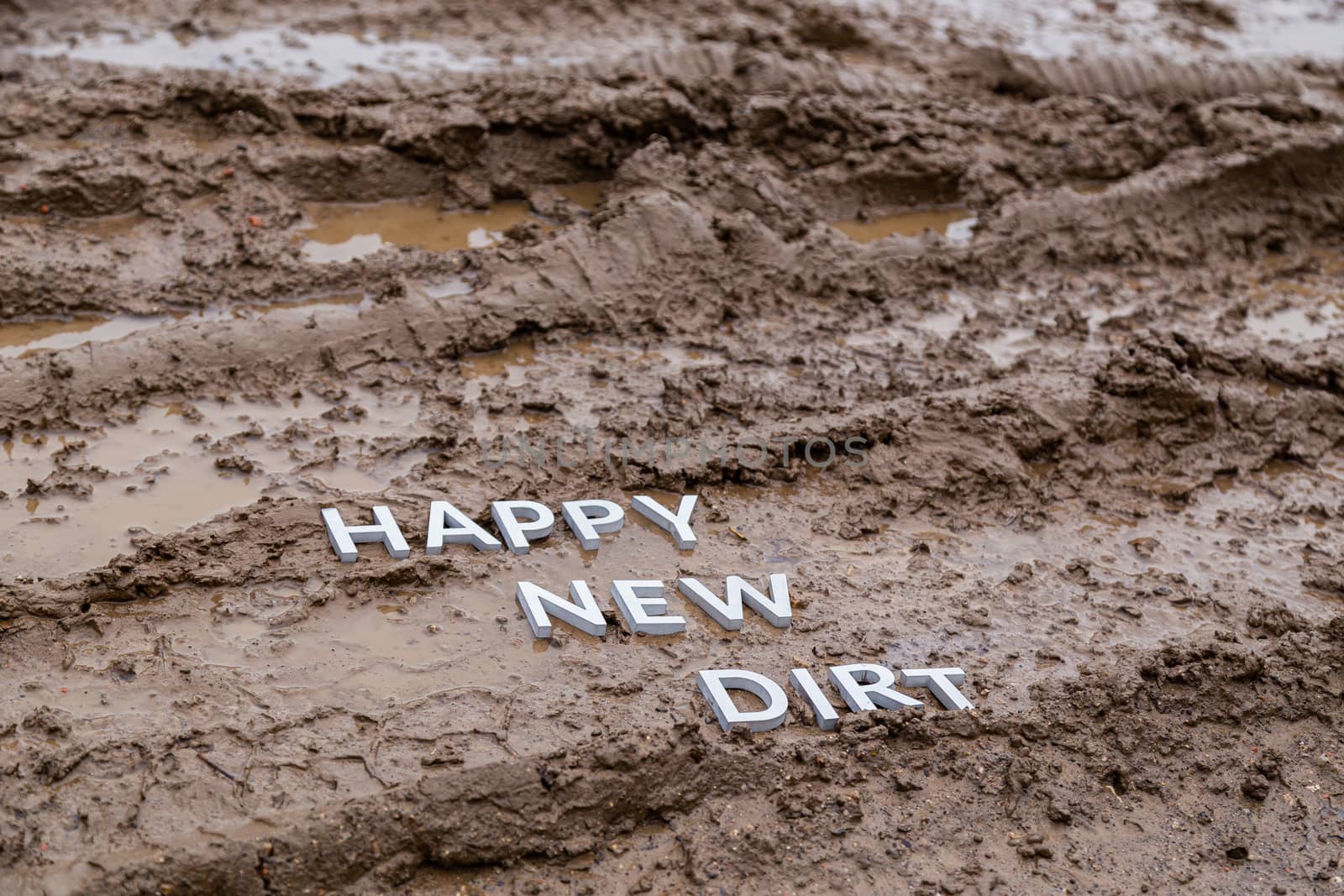 the words happy new dirt laid with silver metal letters on wet mud surface in diagonal perspective under cloudy autumn day light