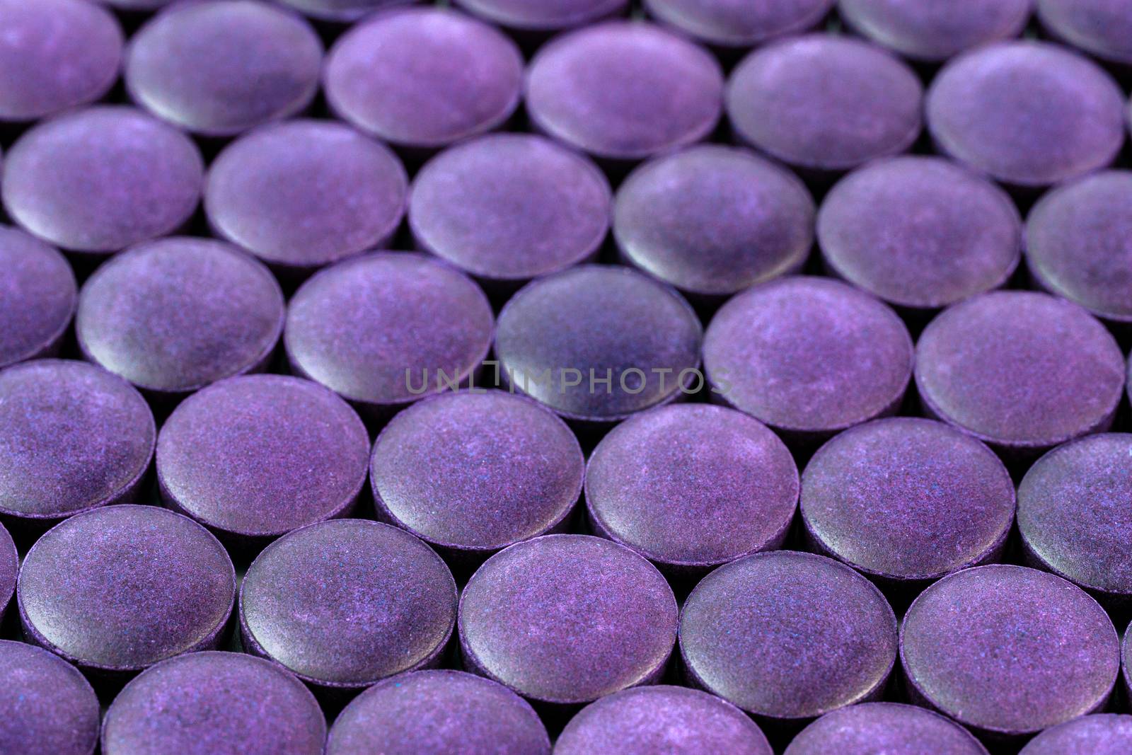 close-up background of many purple organic powder tablets laid tight in one layer on flat surface.