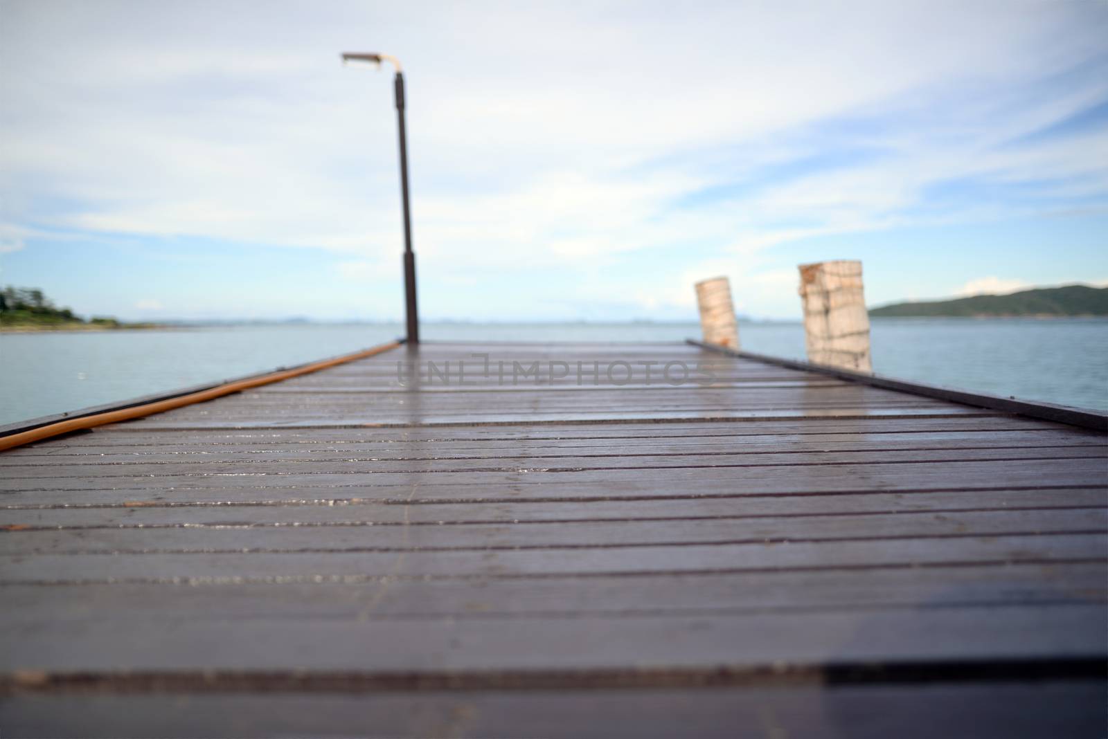 Background picture of a dark brown wooden bridge extending into the sea. There is a blurred background of the sky and the sea. Focus on the middle of the bridge.