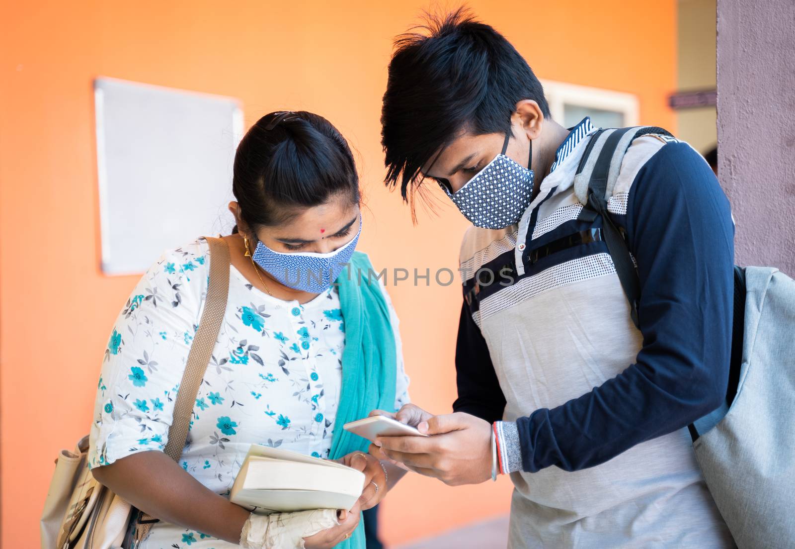University students in medical mask busy on mobile phone at college corridor - concept of students using mobile, technology, Internet and college reopen after covid-19 coronavirus pandemic. by lakshmiprasad.maski@gmai.com