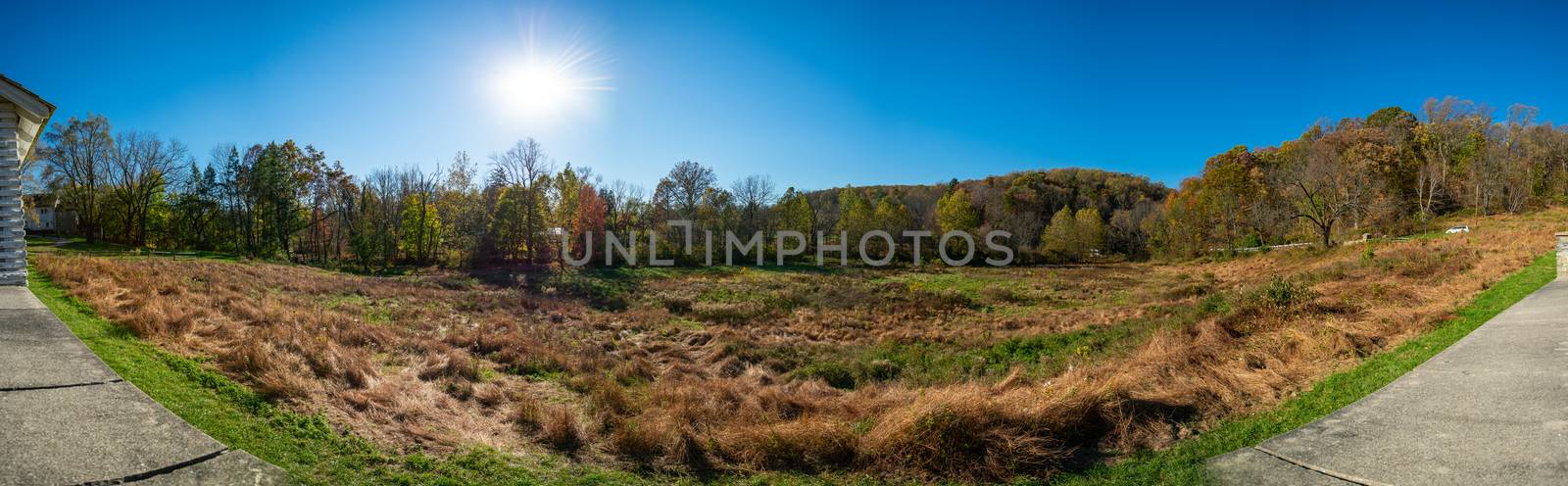 A Panoramic Shot of an Open Field With the Sun Behind Trees at V by bju12290