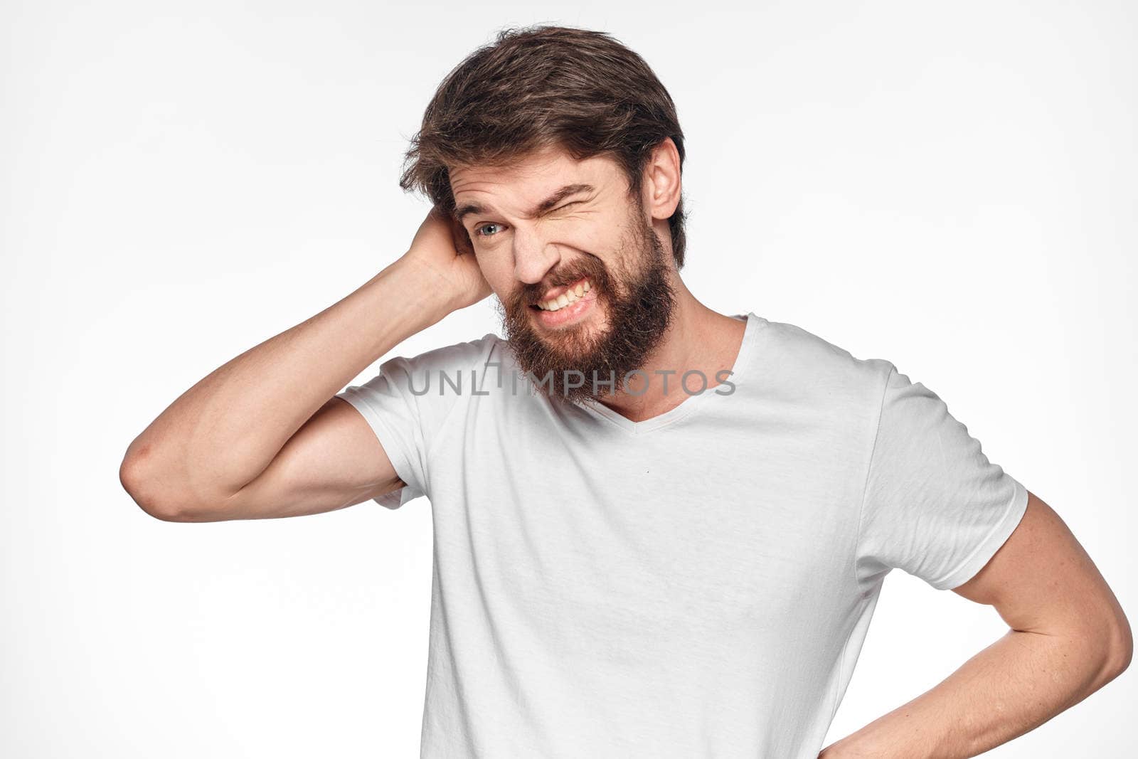 cheerful bearded man in a white t-shirt emotions gestures with his hands light background studio by SHOTPRIME