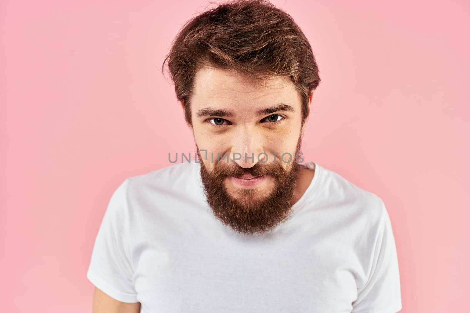 Bearded man in white t-shirt gesturing with hands facial expression close up pink background. High quality photo