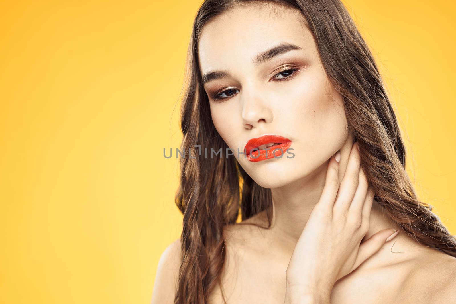 Beautiful brunette naked shoulders bright makeup red lips hairstyle close-up yellow background. High quality photo