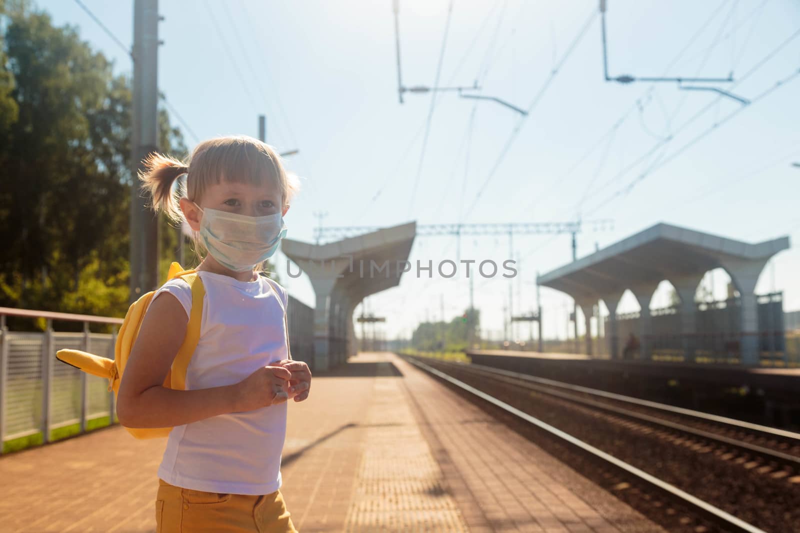 Little girl in a T-shirt and jeans and a medical mask waiting for the train by galinasharapova