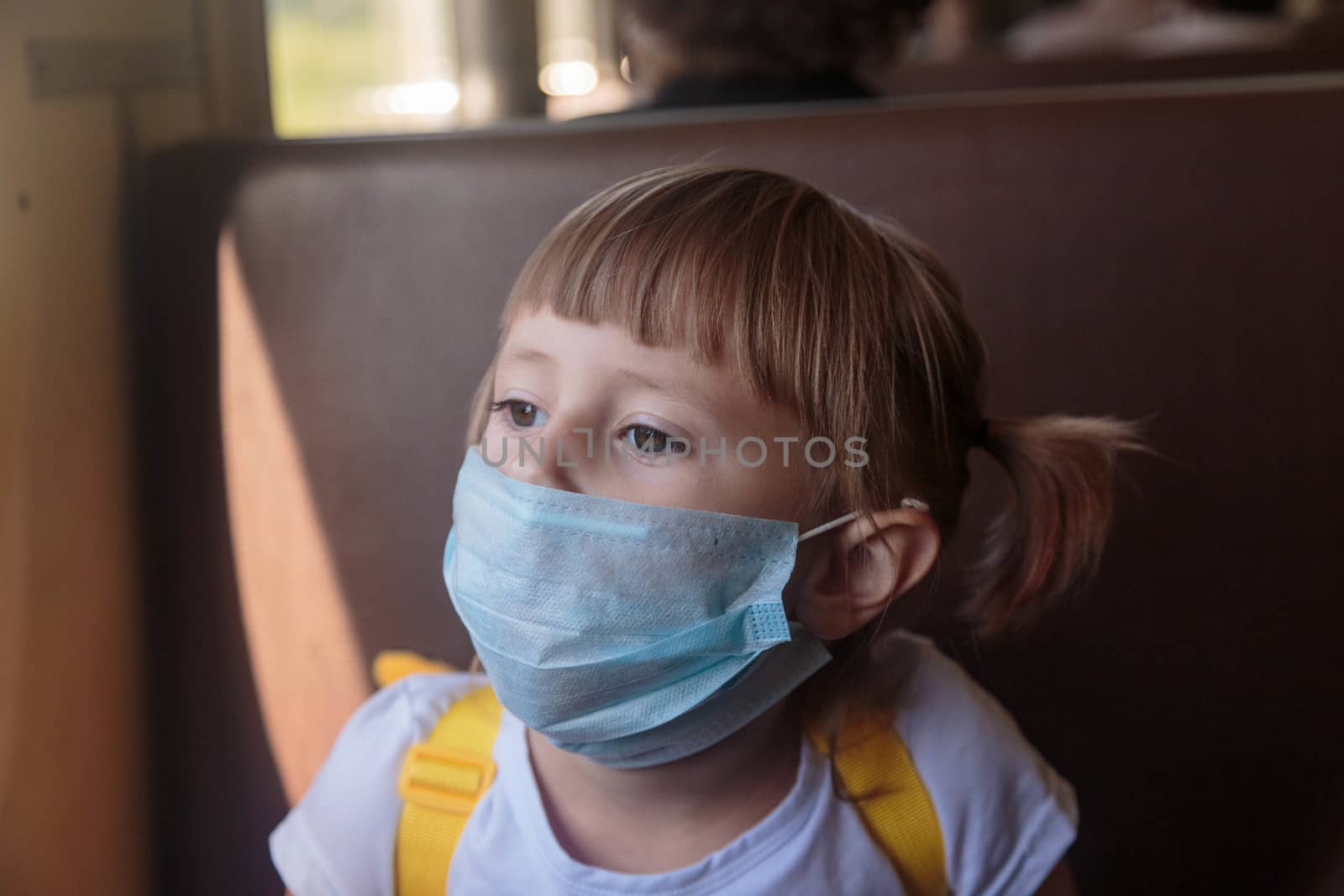 Little girl in a white T-shirt and jeans and a medical mask is sitting in the train. Keep social distancing to avoid the spread of COVID-19. Safe travel.