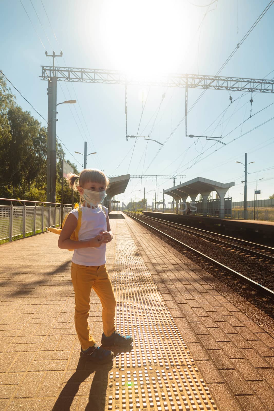 Little girl in a T-shirt and jeans and a medical mask waiting for the train by galinasharapova