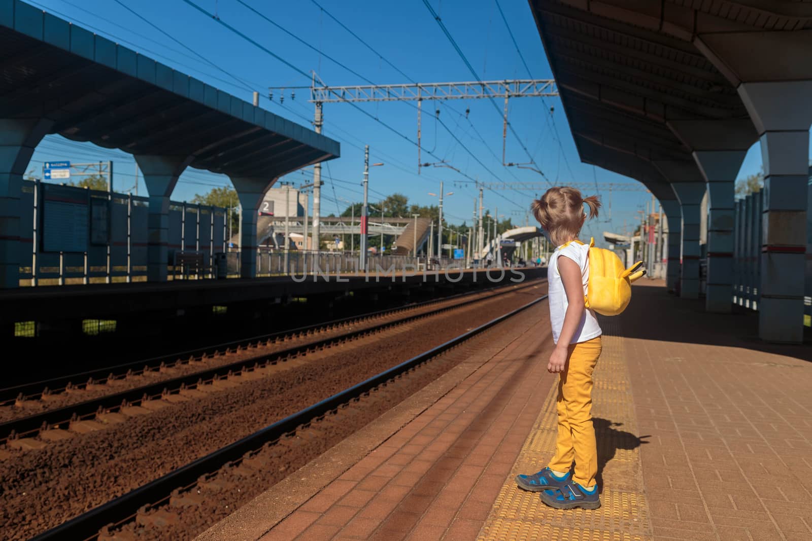 Little girl in a T-shirt and jeans and a medical mask waiting for the train by galinasharapova