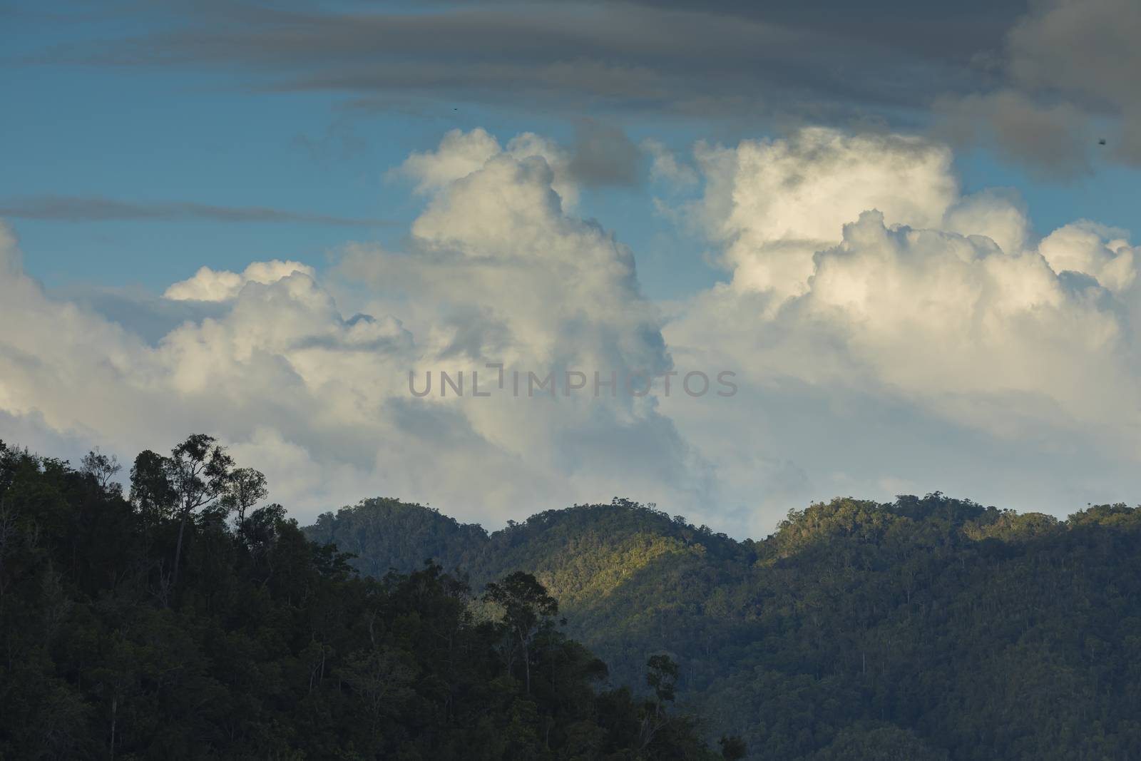 Beautiful clouds and sunset, over the mountains of Waiego Island, covered by thick tropical jungle, in the exotic Raja Ampat Islands, Indonesia, Southeast Asia.