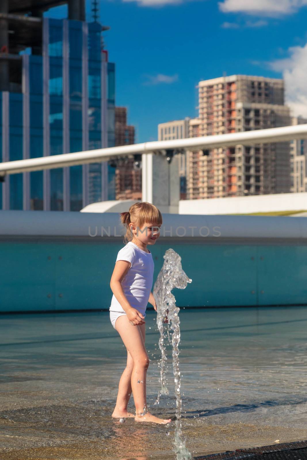 A little girl splashes water from a fountain on the territory of the Moscow city business center