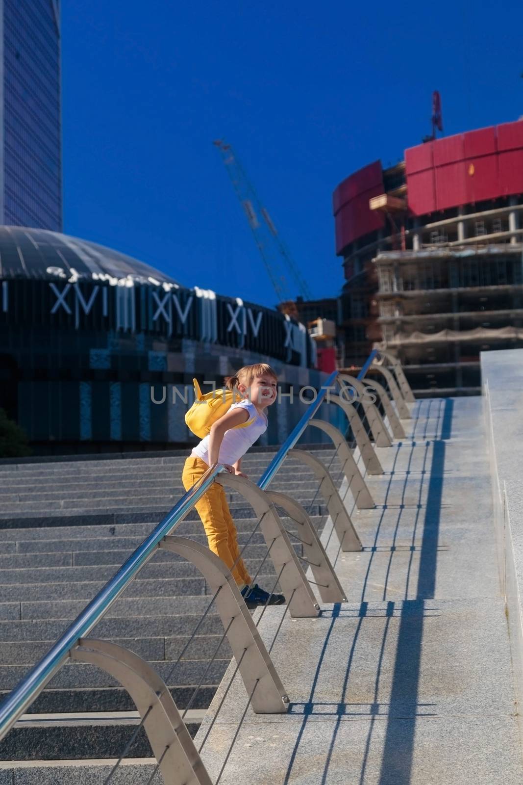 A little girl in yellow jeans stands against the background of the skyscrapers of the business center in Moscow city