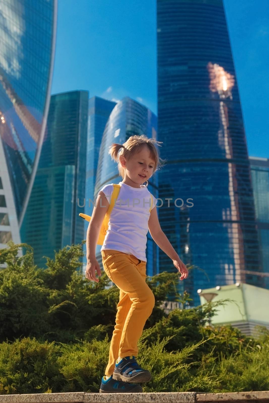 A little girl in yellow jeans stands against the background of the skyscrapers of the business center in Moscow city