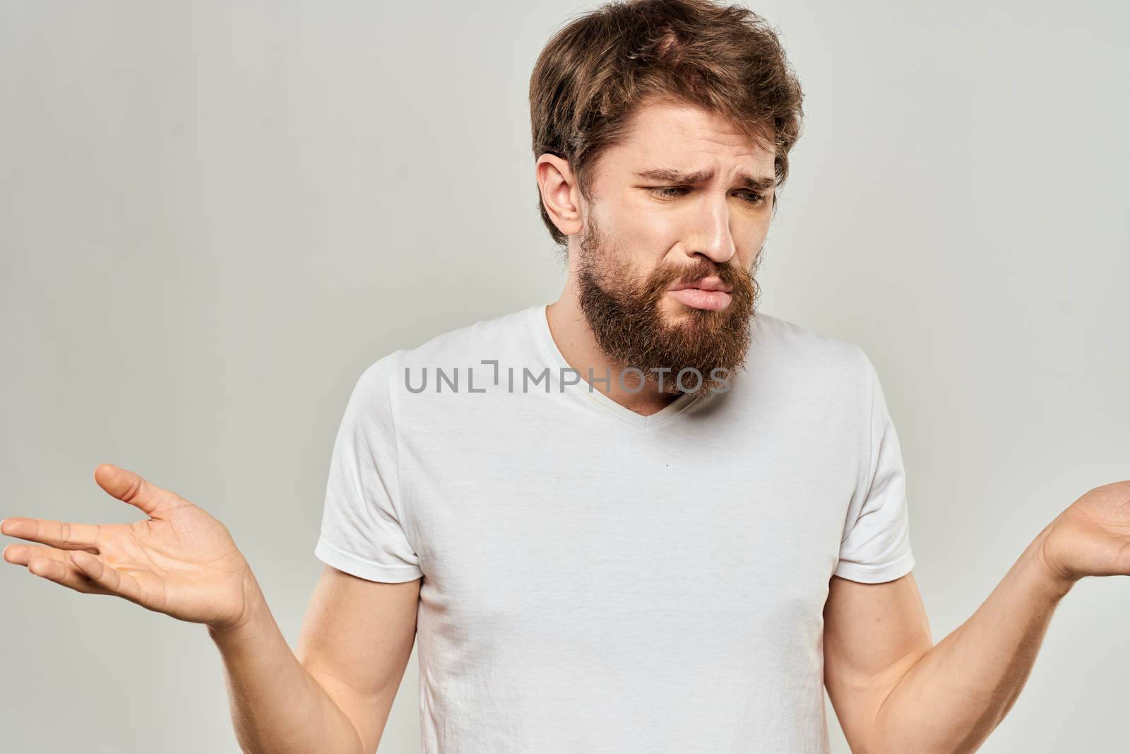 bearded man gesturing with his hands in a white t-shirt aggression light background. High quality photo