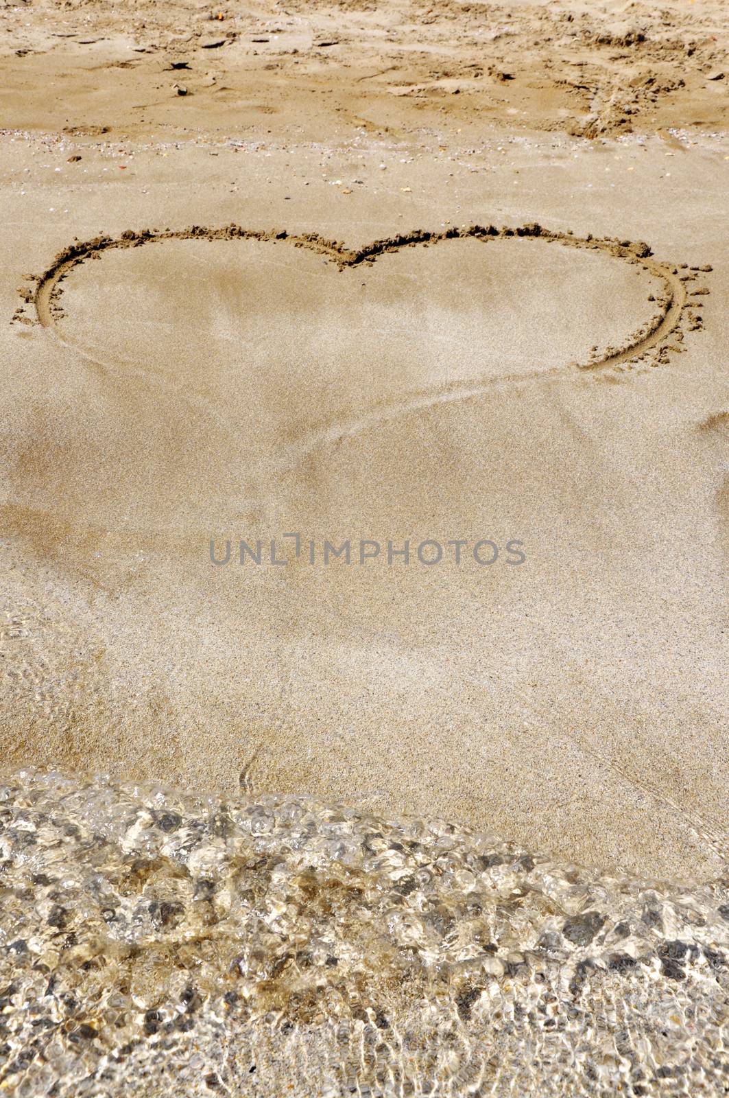 Hand drawn picture of the heart on wet beach sand.