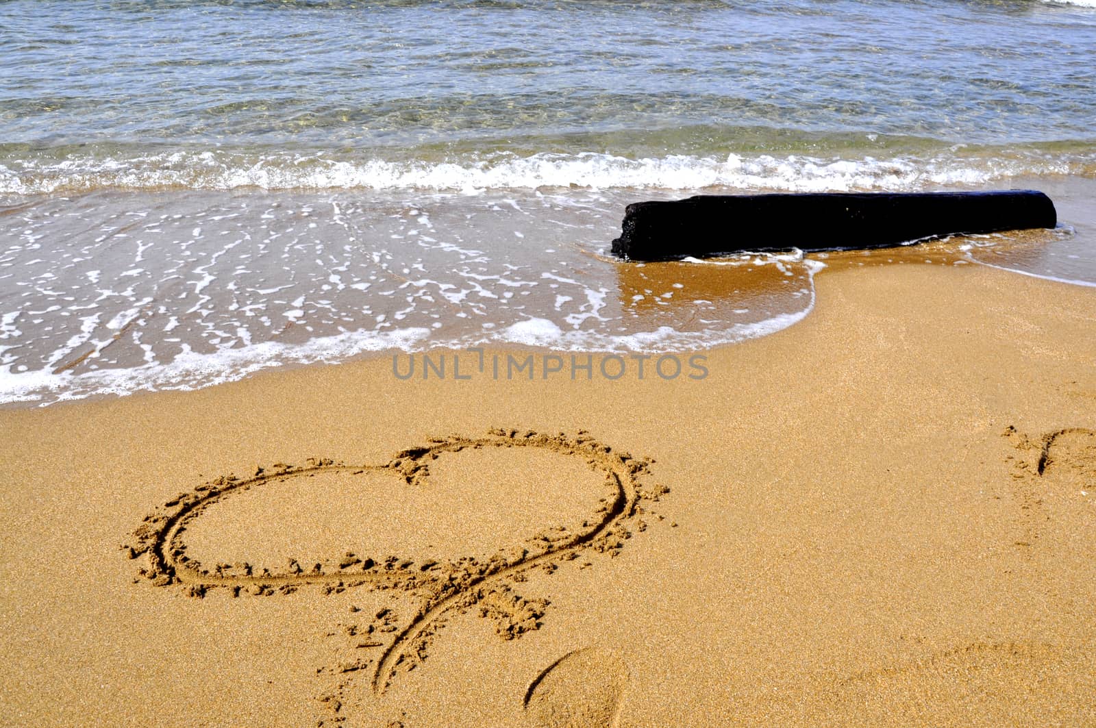 Hand drawn picture of the heart on wet beach sand.