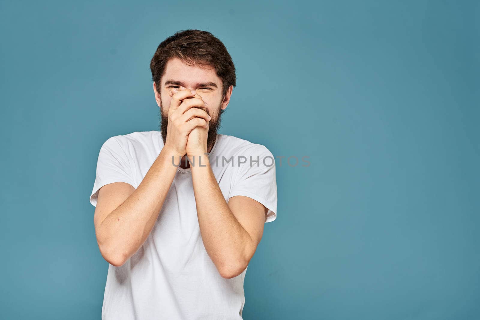 A bearded man in a white T-shirt gestures with his hands emotions blue background by SHOTPRIME