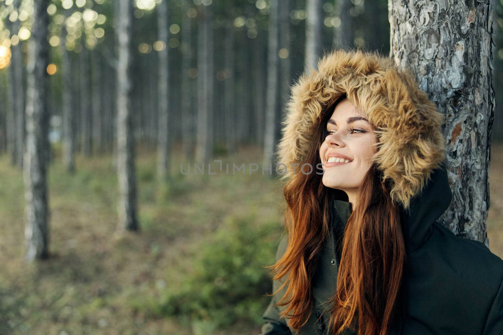 Smiling woman in a jacket in the forest near the travel tree. High quality photo