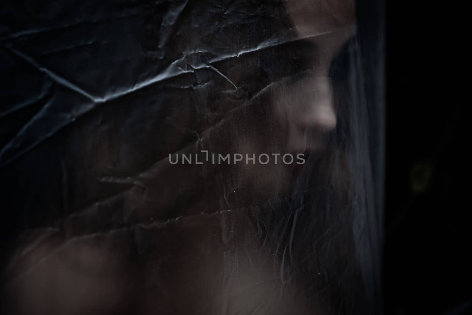 Young beauty sad woman trapped behind a plastic sheet as protection against COVID-19. Nicely fits for book cover