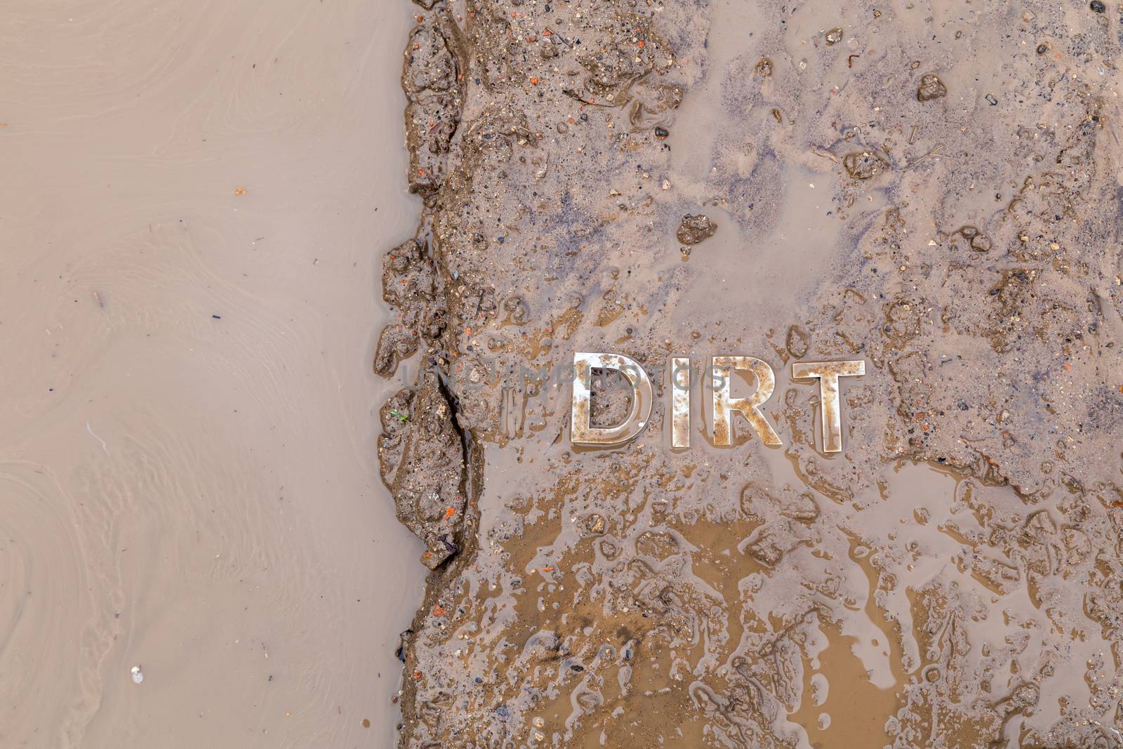 the word mud imprinted in wet dirt road surface and puddle - close-up with selective focus in flat lay perspective.