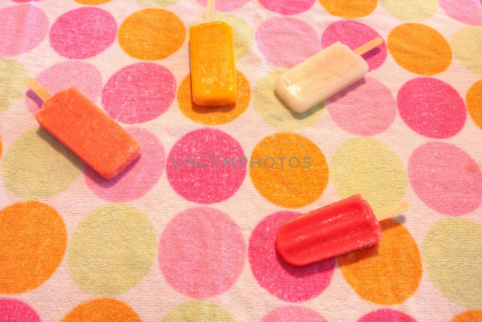 Fruit popsicles on a dotted background in summer including watermelon popsicle, tropical fruit popsicle, mango popsicle, and lime popsicle with fresh raspberries.
