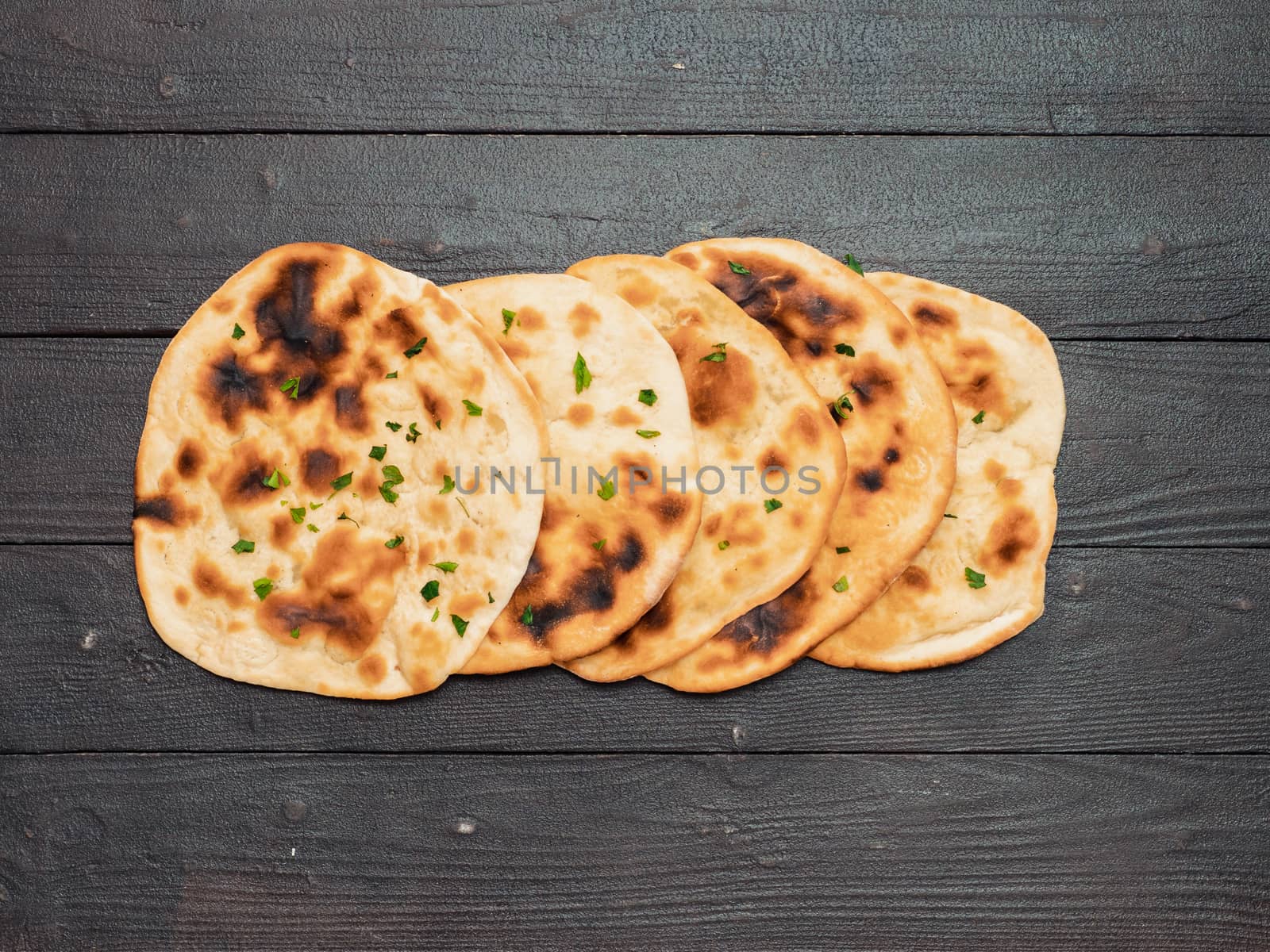 Fresh naan bread on dark wooden background with copy space. Several perfect naan flatbreads top view or flat lay.