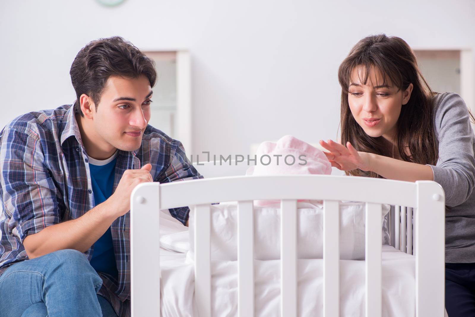 Young parents with their newborn baby near bed cot