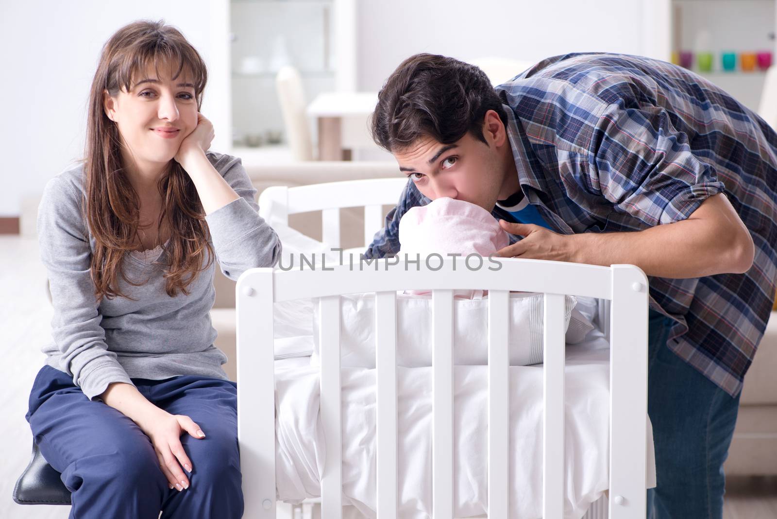 Young parents with their newborn baby near bed cot