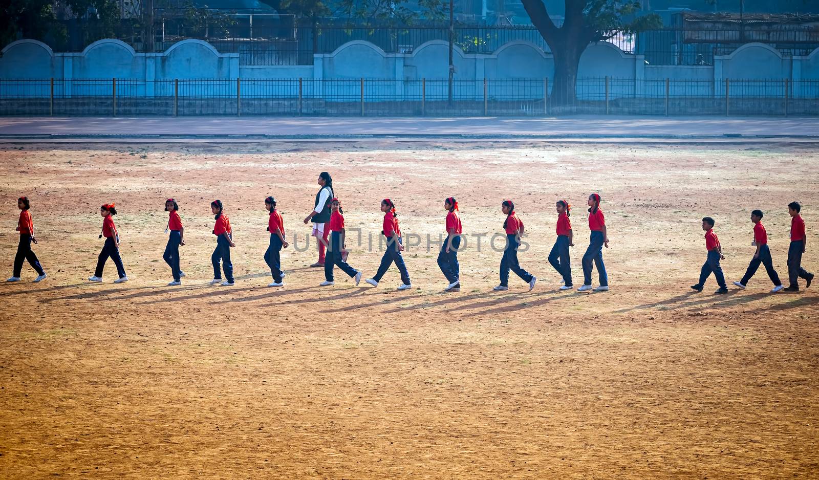 Lady sports teacher guiding children to walk in a formation on playground. by lalam
