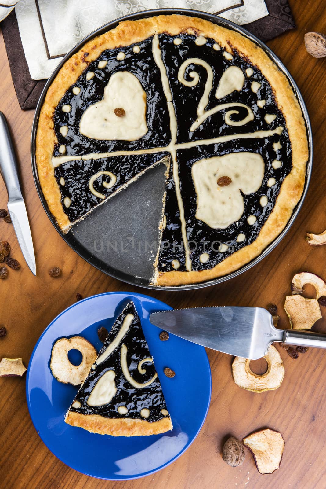 Czech regional traditional hand and home made round pie Chodsky kolac. This one has heart made of quark surounded by plum jam filling. Still life of one slice cut with nuts and fruits around on a wooden table