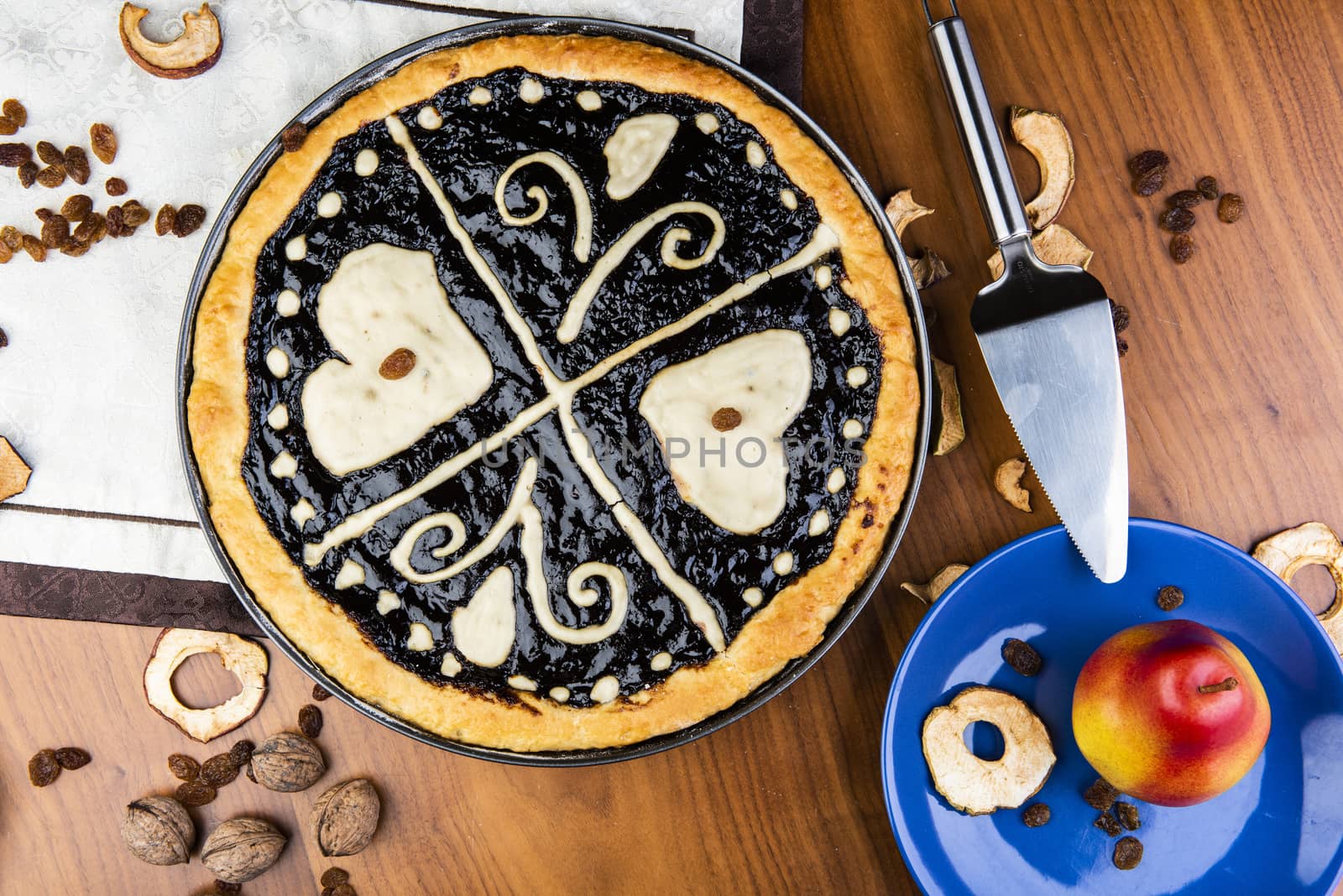 Czech traditional hand and home made round pie Chodsky kolac - speciality of Chodsko region. This one has heart made of quark surounded by plum jam filling. Still life with nuts and fruits on a wooden table