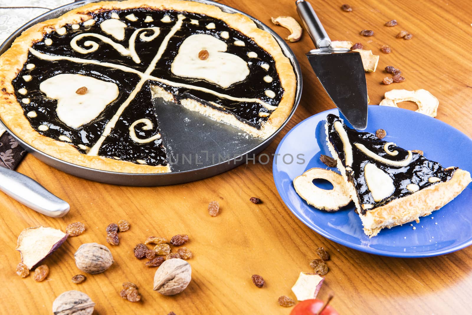 Czech regional traditional hand and home made round pie Chodsky kolac. This one has heart made of quark surounded by plum jam filling. Still life of one slice cut with nuts and fruits around on a wooden table