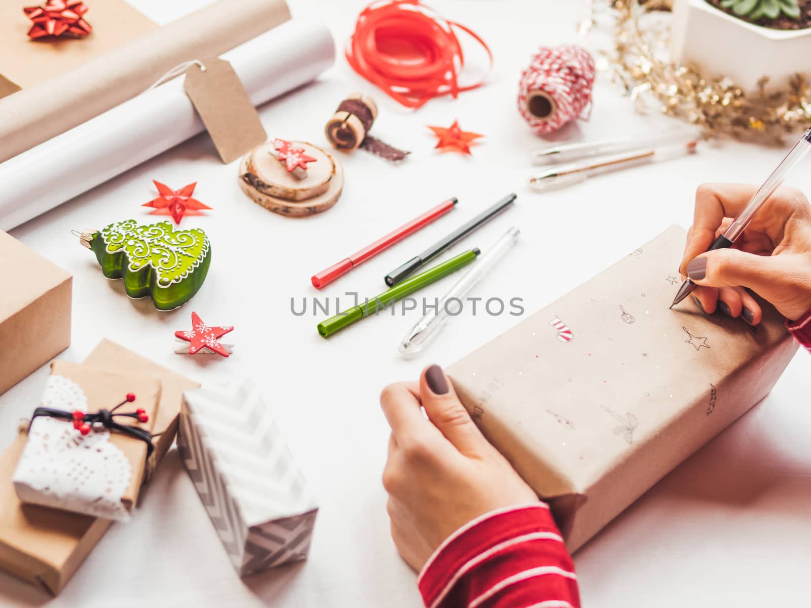 Table with Christmas decorations. Woman draws New Year symbols on craft paper and wraps presents. Flat lay with copy space.