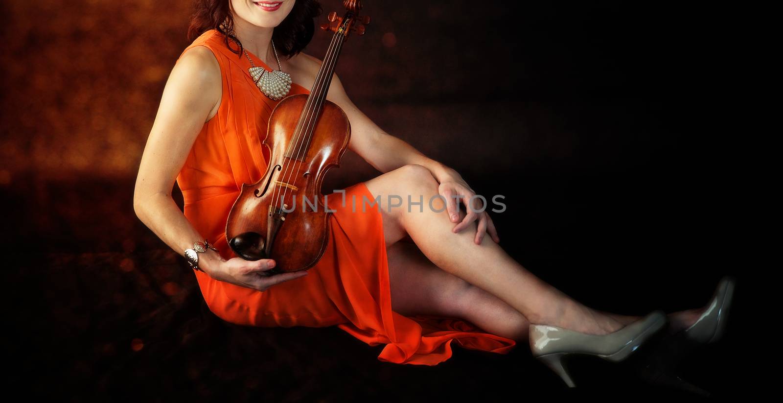 Young woman wearing an elegant orange dress poses with her antique violin