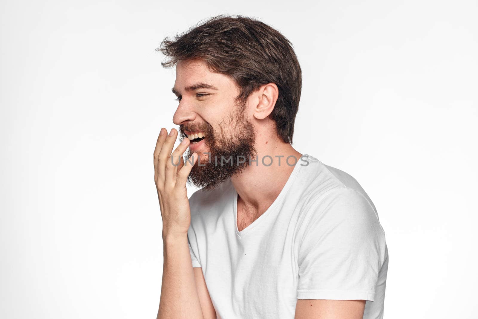 cheerful bearded man in a white t-shirt emotions gestures with his hands light background studio. High quality photo