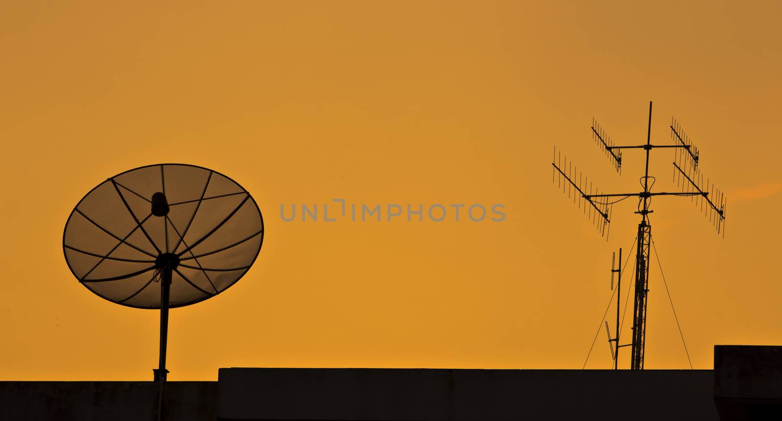 Satellite and antenna on roof in the sunset.
