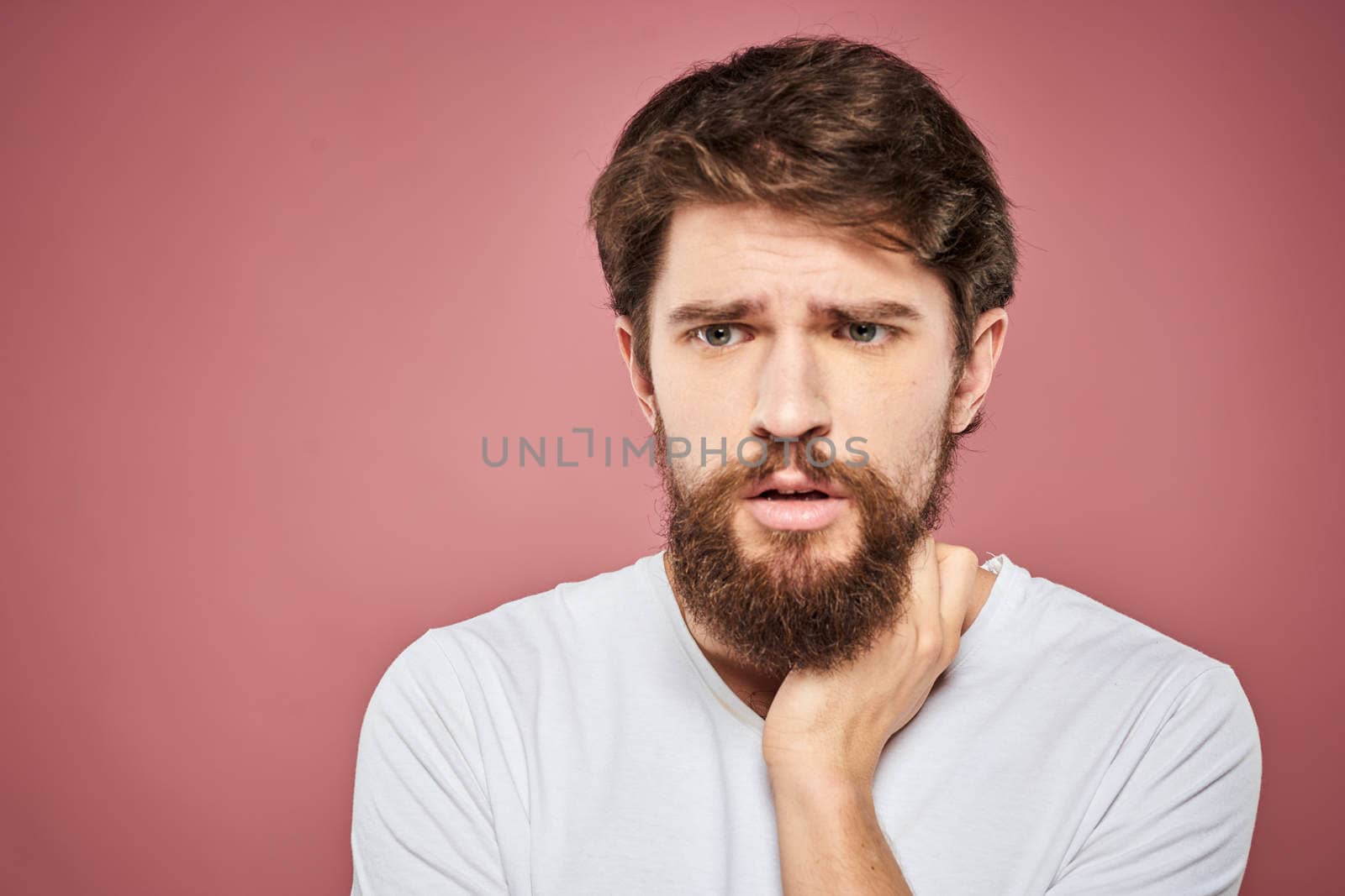 Emotional bearded man in white T-shirt discontent pink background. High quality photo