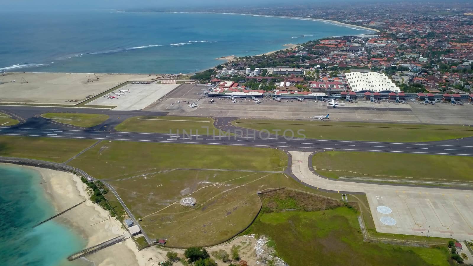 Aerial view of the runway from the top of the tower of the international airport controls Bali with a parked plane and several planes are on the runway. Aerial view to Ngurah Rai airport, Indonesia.