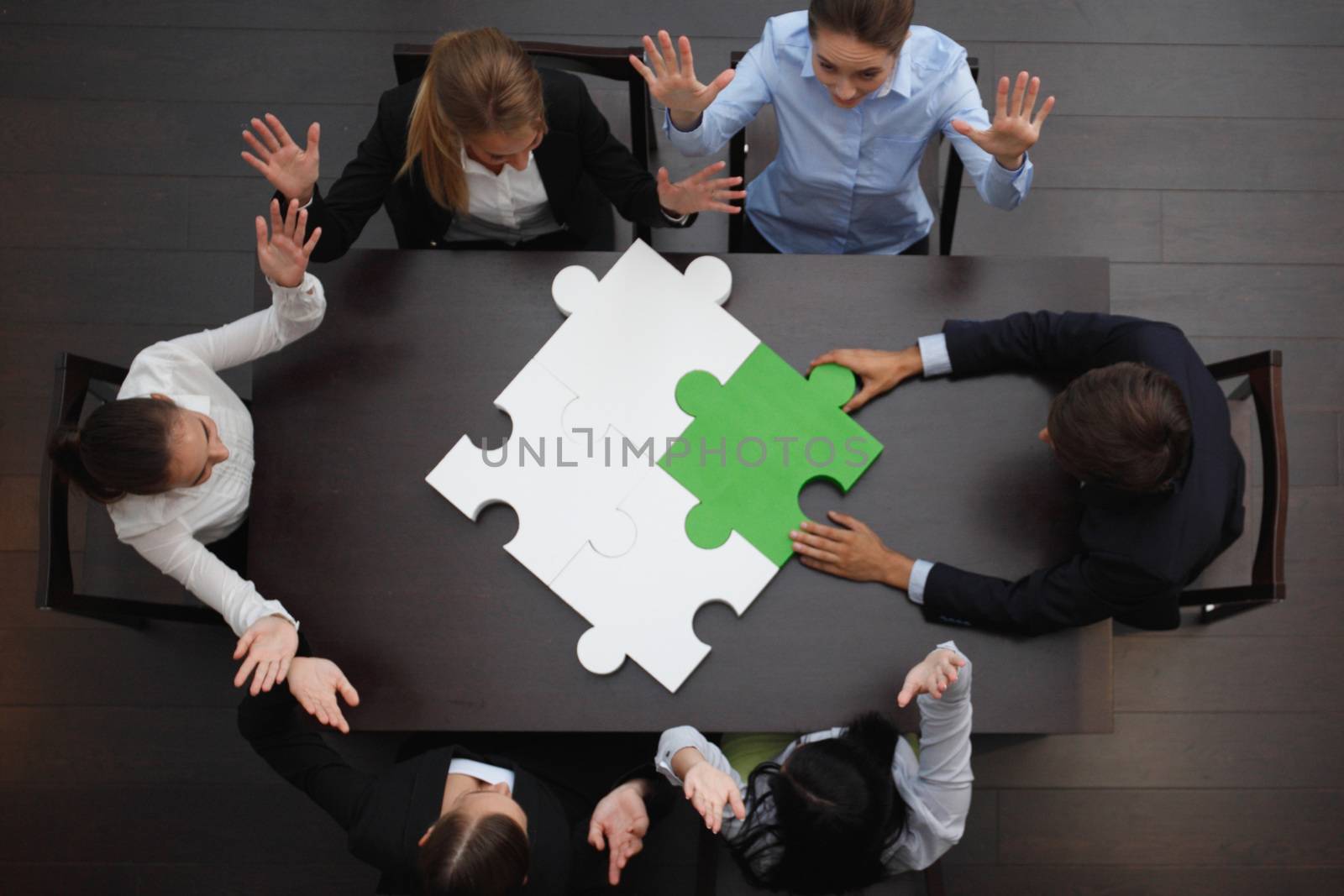 Group of business people assembling jigsaw puzzle at office table, top view, team support and help concept, green and white pieces