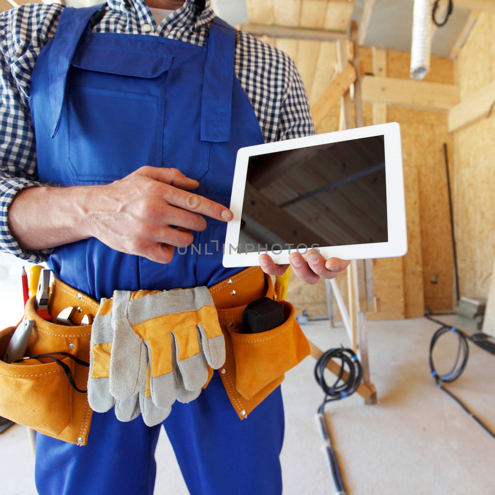 Constructor male worker pointing tablet with empty screen and copyspace isolated at construction site background