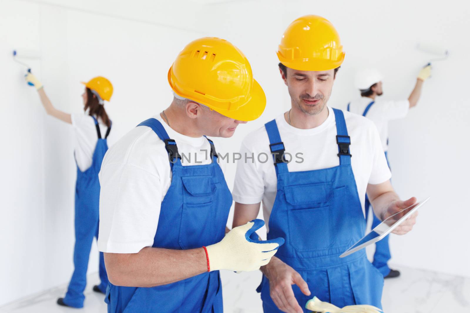 Workers in blue uniform and yellow hardhats with blueprint working at construction site