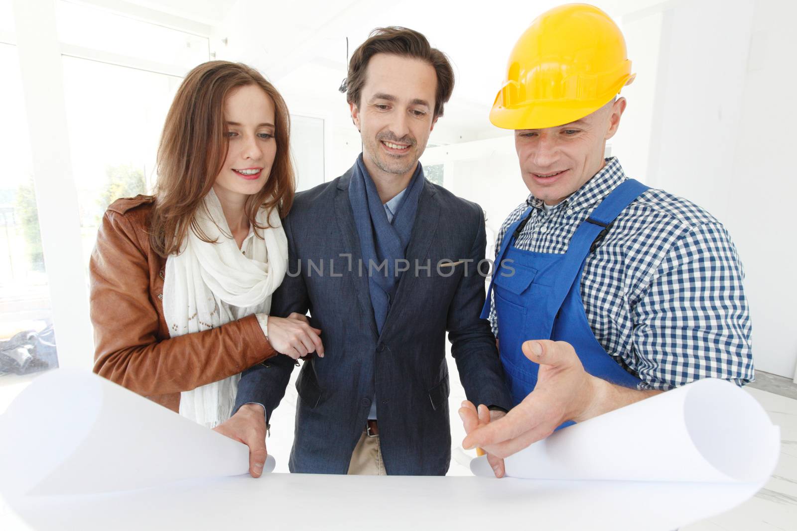 Foreman showing house design construction plan to a happy young couple new house real estate concept