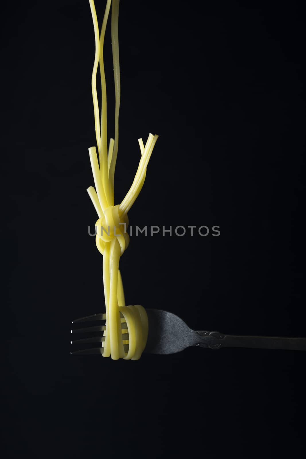 Spaghetti on a fork in front of black background.