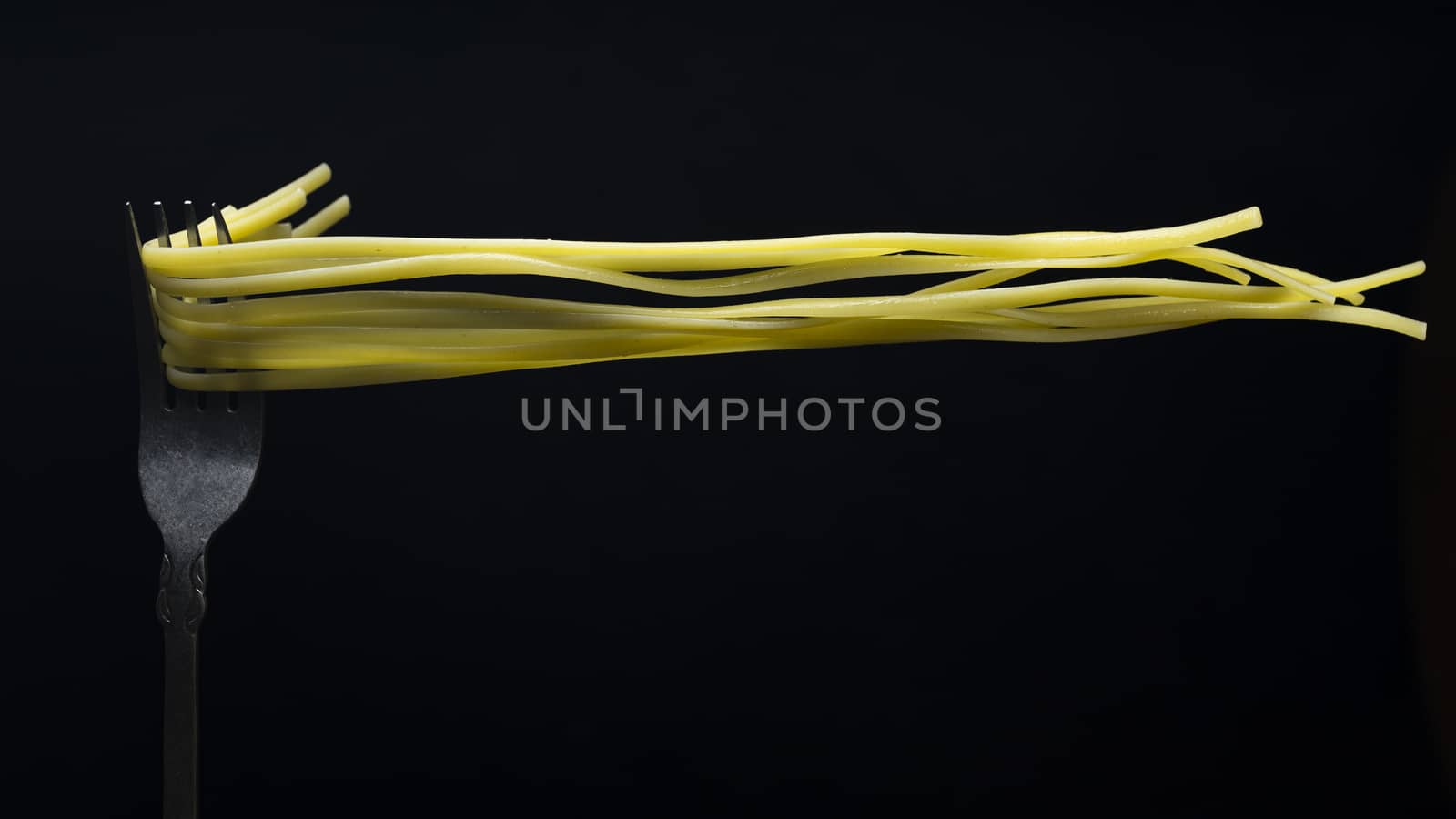 Spaghetti on a fork in front of black background.