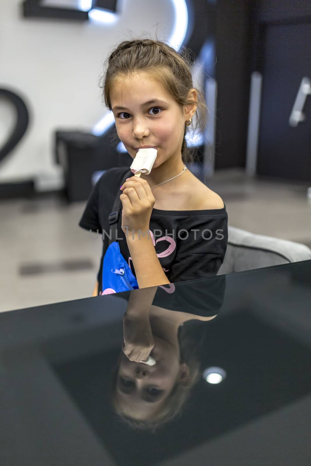 02.09.2019 Kiev, Ukraine. Beautiful girl with big eyes eating ice cream, she is reflected in a black shiny table